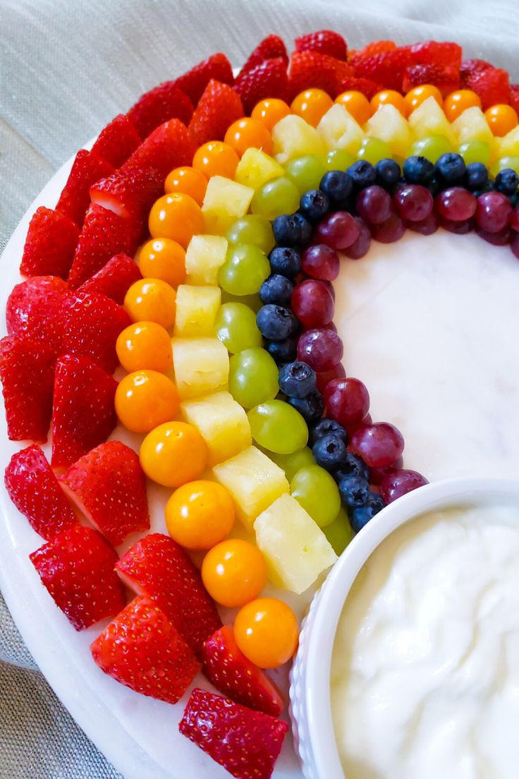 a white plate topped with fruit covered in yogurt next to a rainbow cake