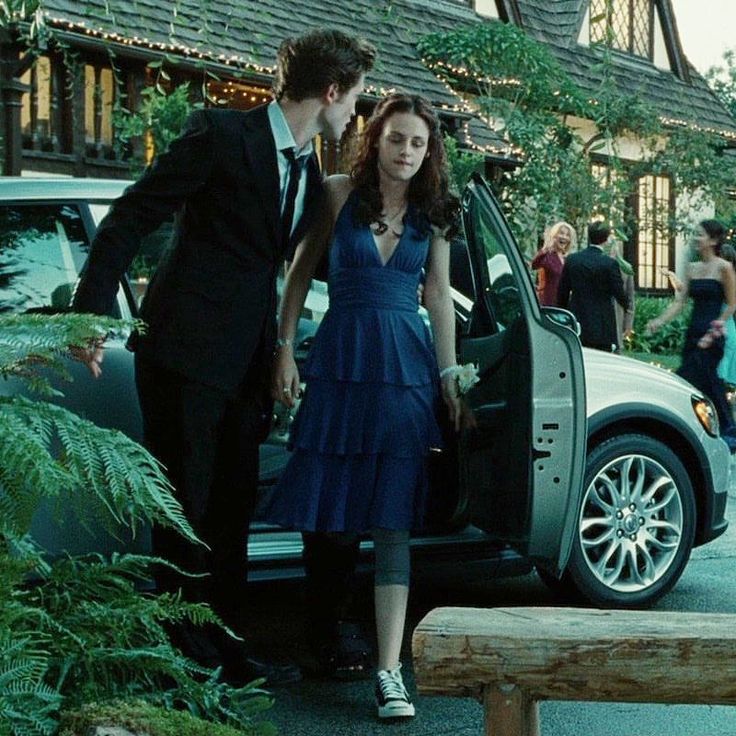 a young man and woman standing next to a parked car in front of a house