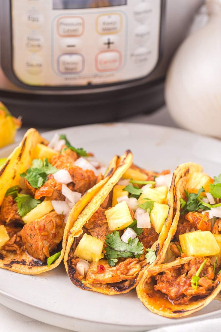 three tacos on a plate next to an instant pot roaster