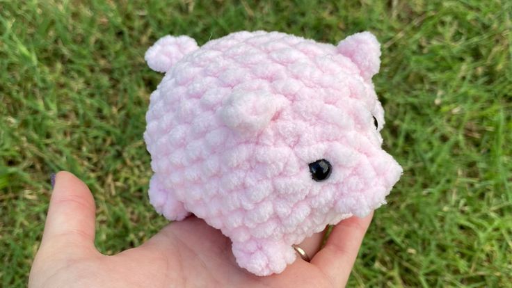 a hand holding a small pink crocheted teddy bear in the middle of grass