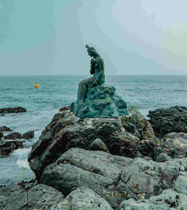 a statue sitting on top of a rock next to the ocean