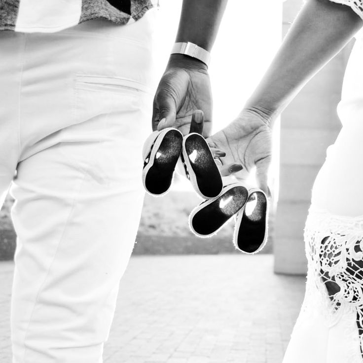 a man and woman holding hands while standing next to each other on a sidewalk with their shoes in the air