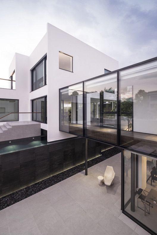 a house with glass walls and stairs leading up to the upper floor, which also has an outdoor swimming pool