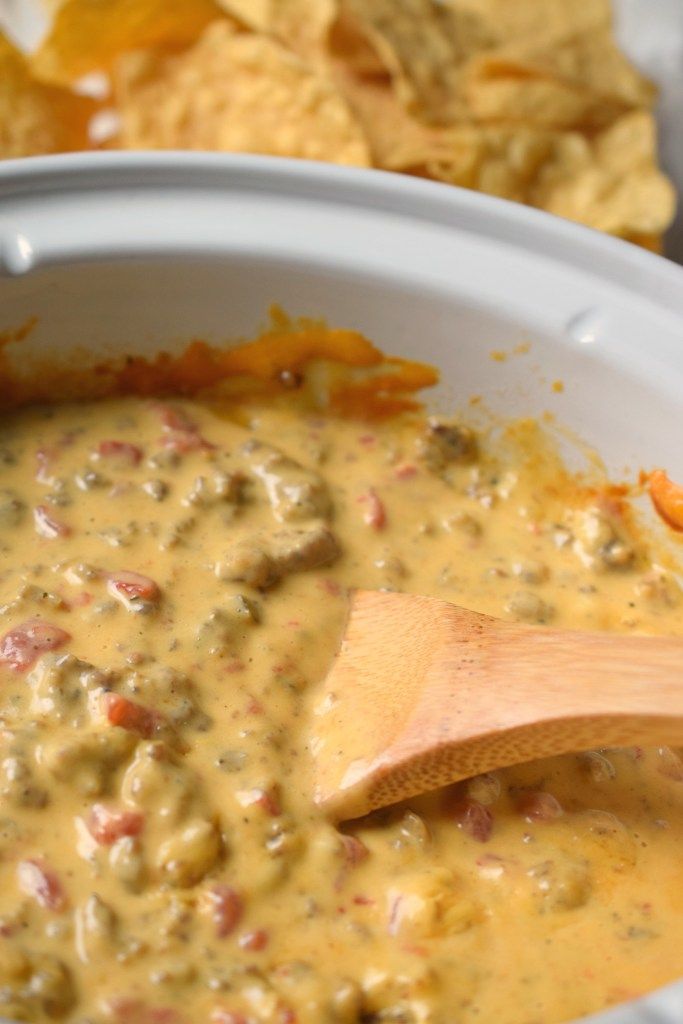 a wooden spoon in a white bowl filled with cheese and tortilla chips on the side