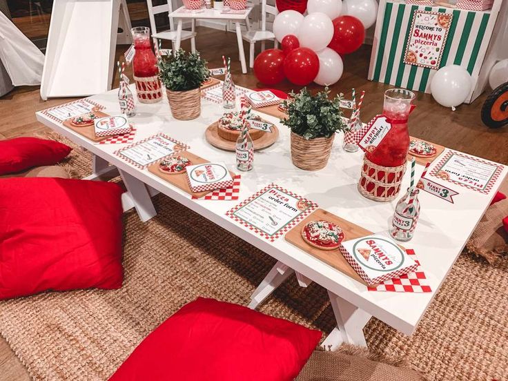 a table set up for a party with red and white decorations, balloons and food