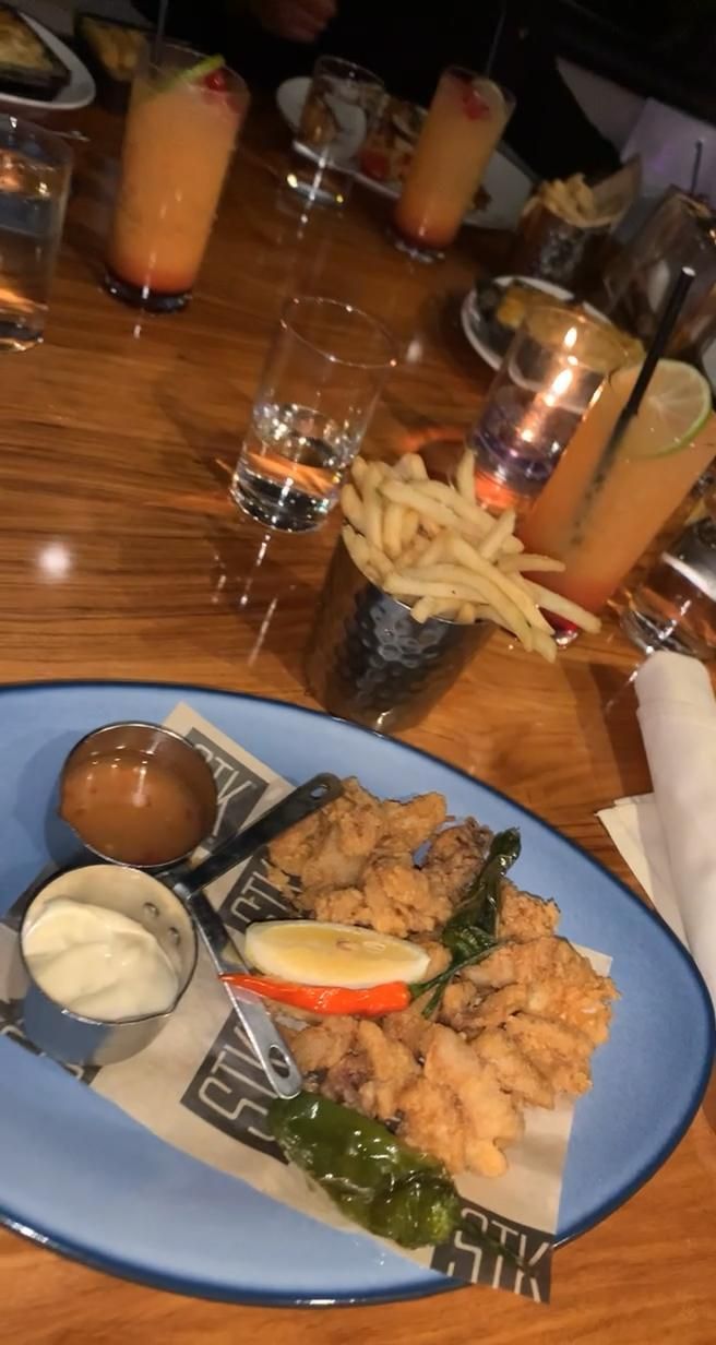 a blue plate topped with fried food on top of a wooden table next to drinks