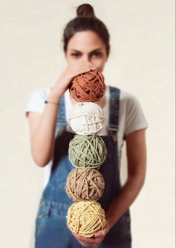 a woman in overalls holding balls of yarn over her face and covering her mouth