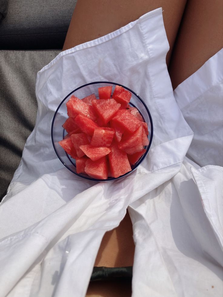 a bowl full of watermelon slices sitting on top of a white cloth next to a person's legs