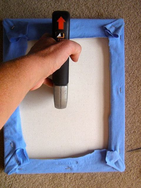 a hand is holding a remote control in front of a square frame with blue fabric