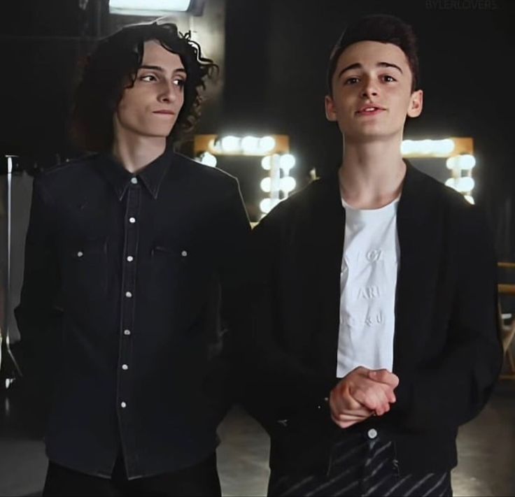 two young men standing next to each other in front of a mirror with lights behind them