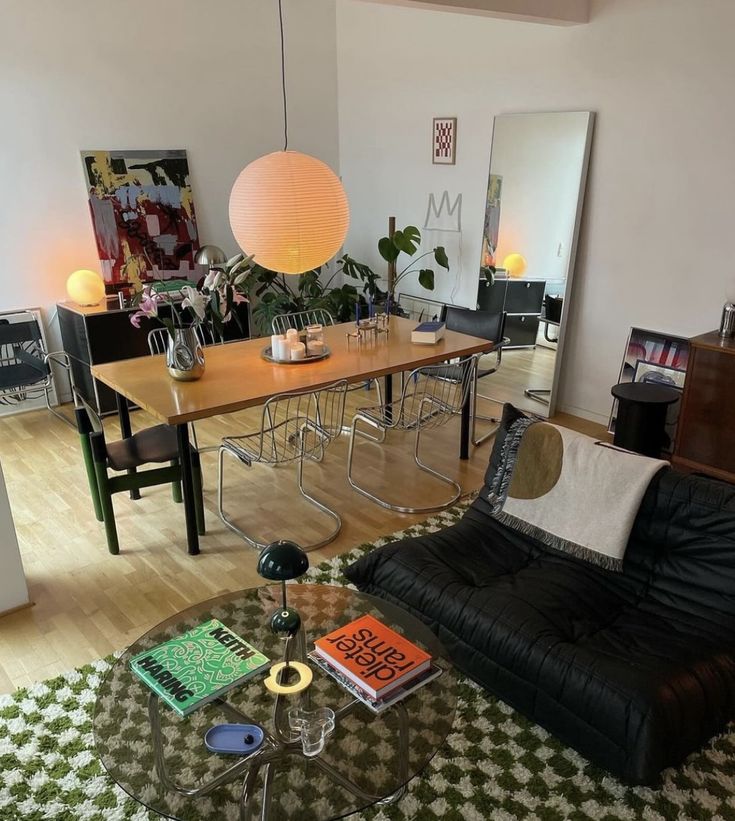 a living room filled with furniture next to a dining room table and two lamps hanging from the ceiling