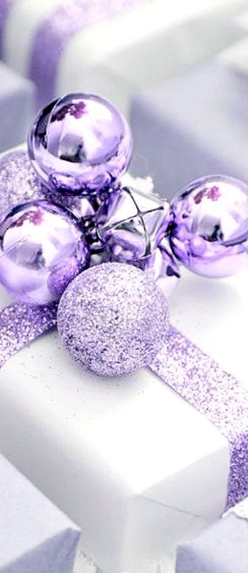 purple and silver ornaments are on top of a white present box with glitter ribbon around it