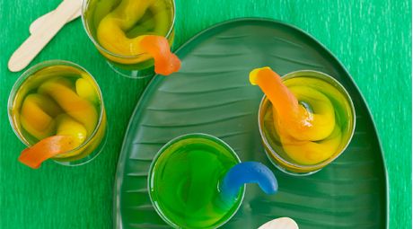 three cups filled with different colored jello sitting on top of a green plate next to spoons