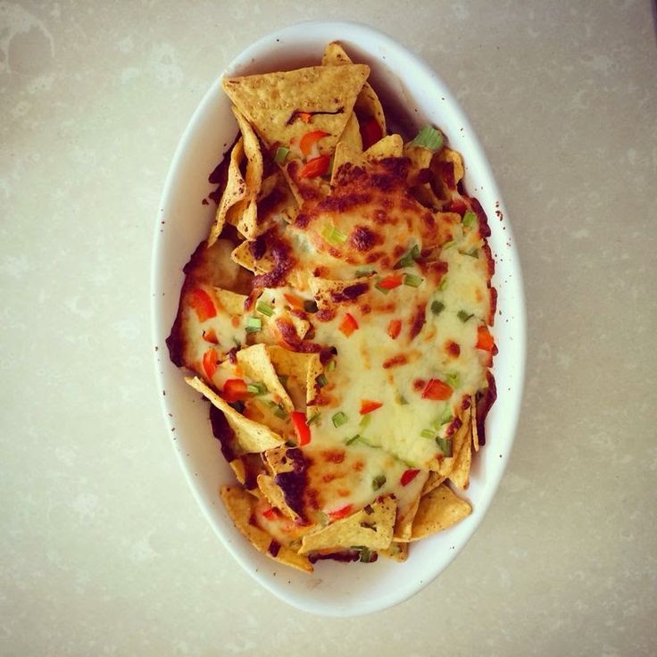 a white bowl filled with nachos and cheese on top of a table next to chips