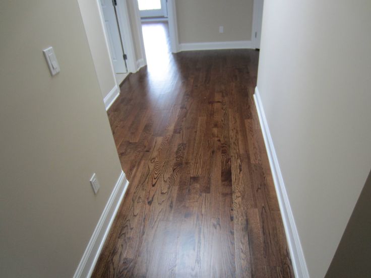 an empty hallway with hard wood flooring and white trim on the walls, leading to a door