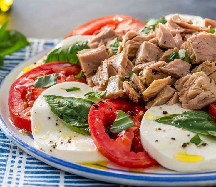 a plate filled with meat and tomatoes on top of a blue and white table cloth