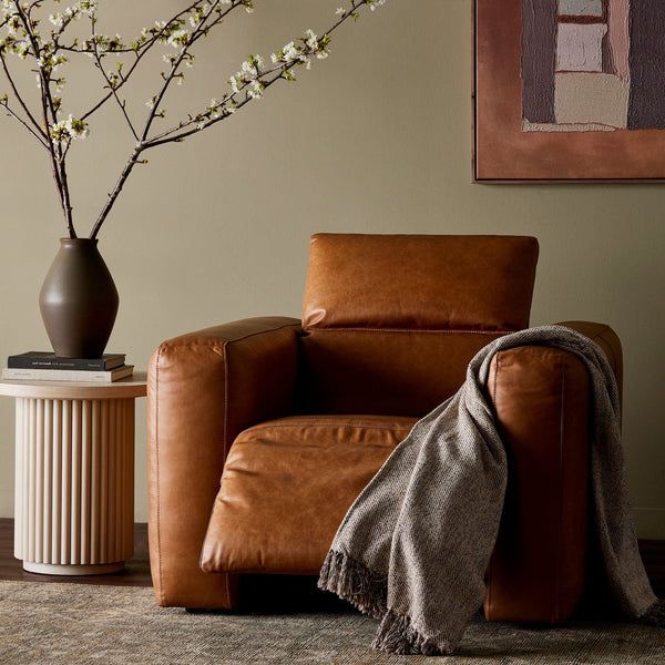 a brown leather chair sitting next to a vase with white flowers on top of it