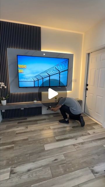 a man kneeling down in front of a flat screen tv on a wall mounted above a wooden floor