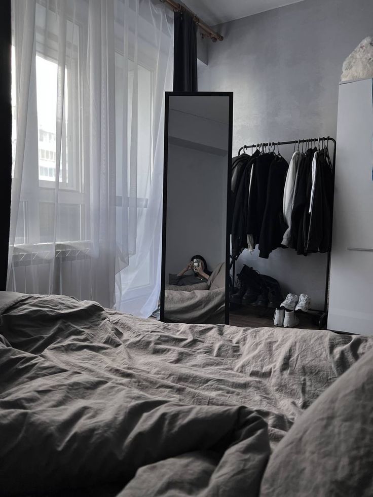 a bedroom with a bed, mirror and clothes hanging on the wall in front of it