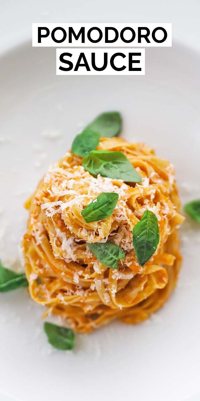 a white plate topped with pasta covered in sauce and garnished with green leaves