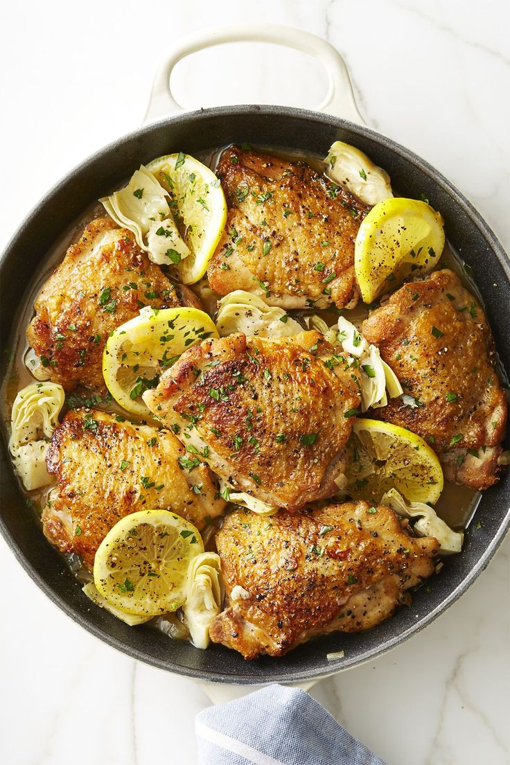 chicken with lemons, onions and herbs in a skillet on a marble countertop