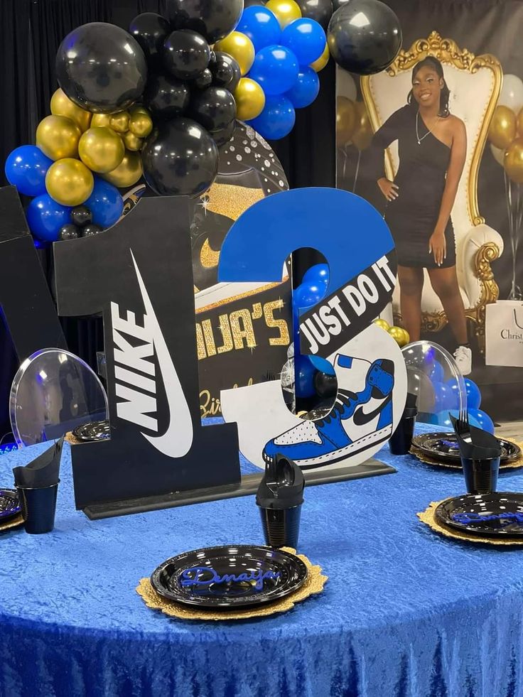 a blue table topped with black and gold plates next to balloons in the shape of letters