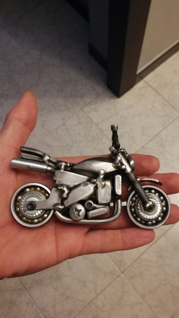 a metal model of a motorcycle in someone's hand on the floor next to a tile floor