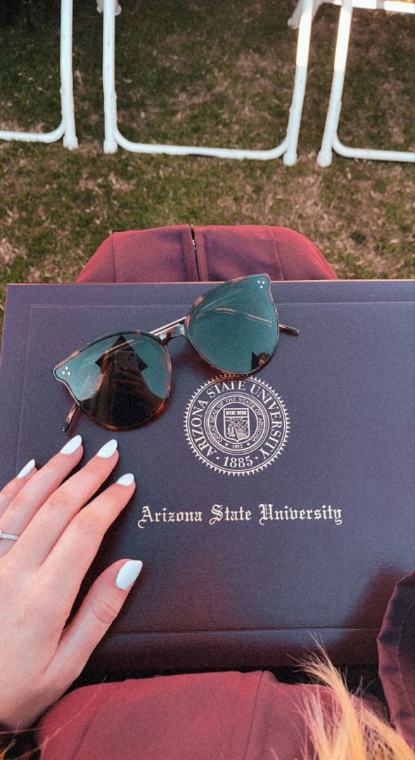 a pair of sunglasses sitting on top of an arizona state university book next to a woman's hand