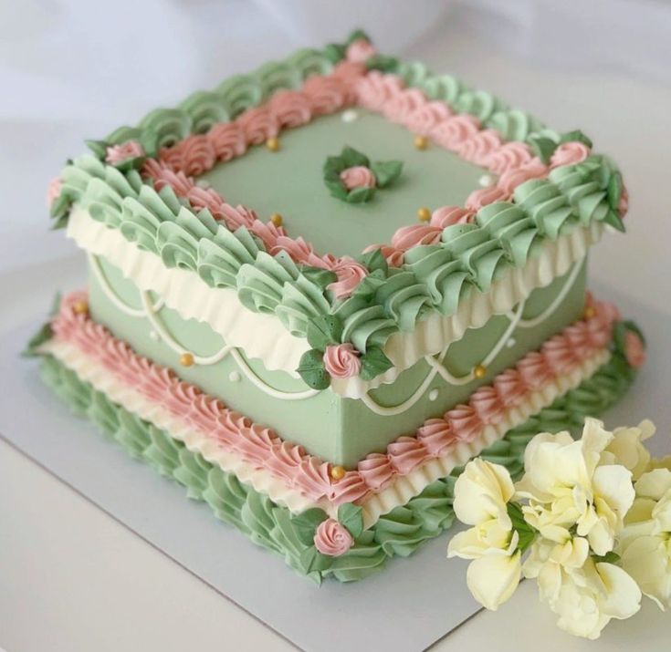 a three layer cake with green frosting and pink icing on the top, sitting next to a white flower