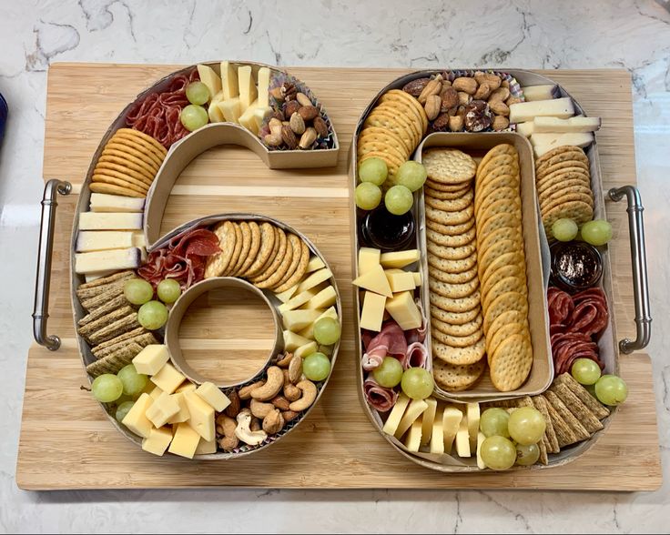 the number 50 made out of crackers, grapes, nuts and cheese on a cutting board