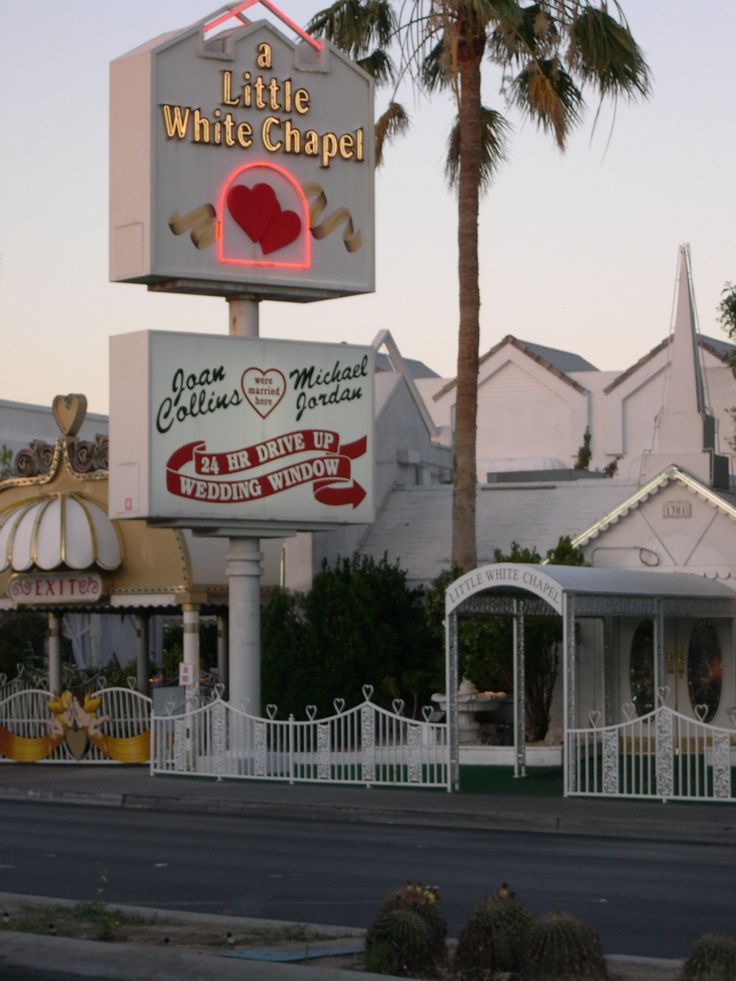 a sign for a little white chapel with palm trees in the foreground and houses in the background