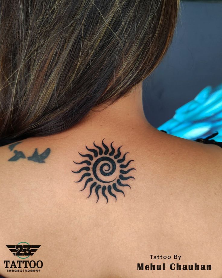 the back of a woman's neck with a sun tattoo on her left shoulder