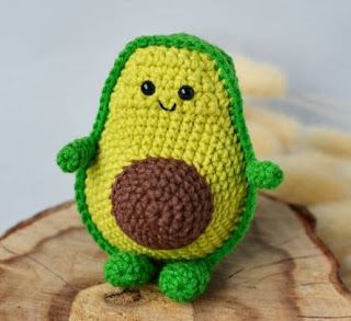 a small crocheted avocado sitting on top of a tree stump next to bananas