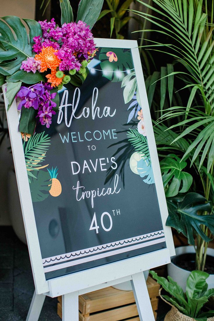 a welcome sign with flowers and greenery on it