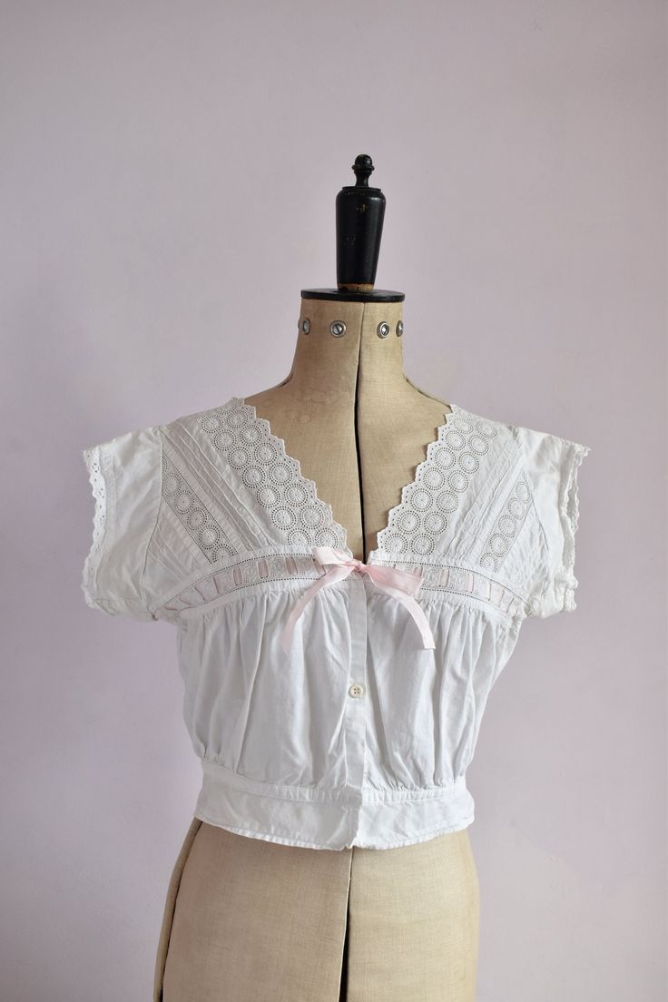 Vintage antique Victorian cotton cover blouse. Embroidered floral pattern on yoke. Scalloped neckline and around arm holes. Drawstring bust with pink ribbon. Plastic button down the front. Cinches in at the waistband with peplum. Excellent vintage condition.  Size small. Measurements:  Strap to strap: 16" Bust: 35" Waist: 26" at waistband at last fastening could be worn open up to 28" comfortably Length: 17" from top of shoulder Vintage Cotton V-neck Blouse, Vintage Lace Trim Camisole Top, Vintage Camisole Top For Daywear, Vintage Fitted Tops With Broderie Anglaise, Fitted Vintage Cotton Lace Tops, Broderie Anglaise Lace Top For Daywear, Fitted Broderie Anglaise Top For Daywear, Fitted Cotton Lace Top With Ruffles, Feminine Cotton Lace Top With Lace Trim