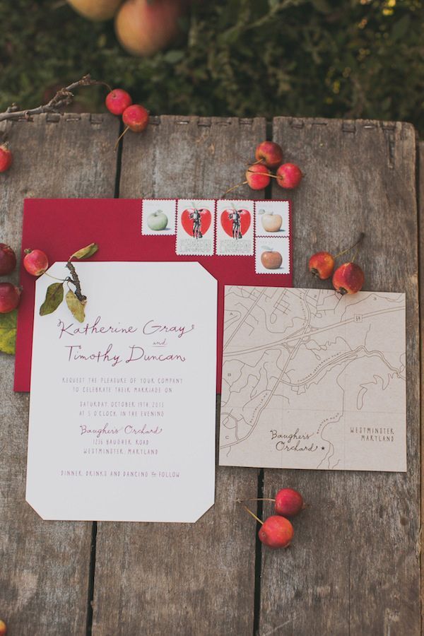 the wedding stationery is laid out on an old wooden table with apples around it