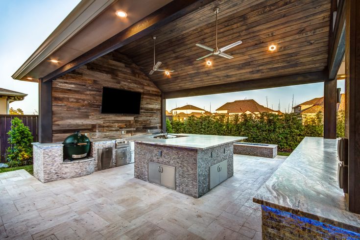 an outdoor kitchen with grill and television on the wall