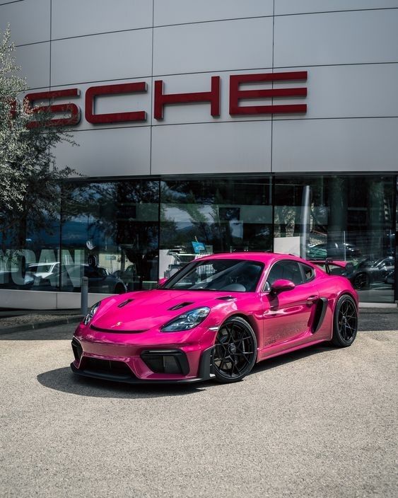 a pink sports car is parked in front of a porsche dealership with its name on it