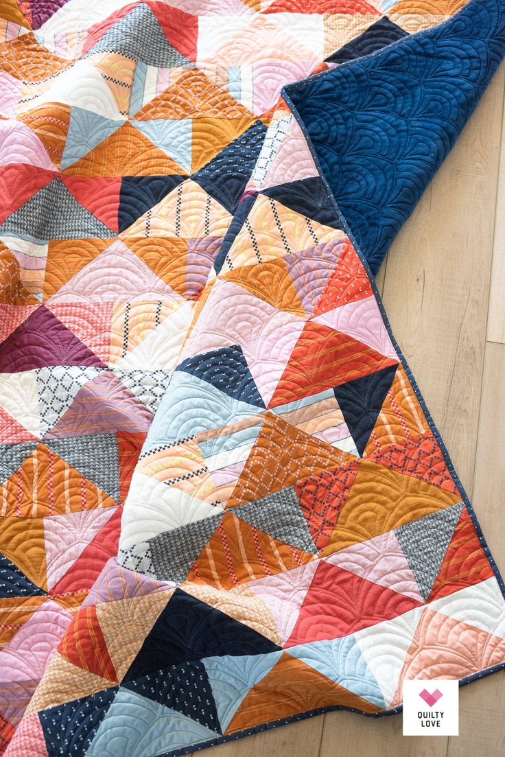 a colorful quilt is laying on the floor with it's blue and orange colors