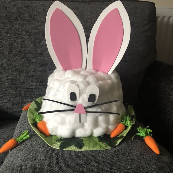 an easter bunny made out of foam sitting on top of a gray couch next to carrots