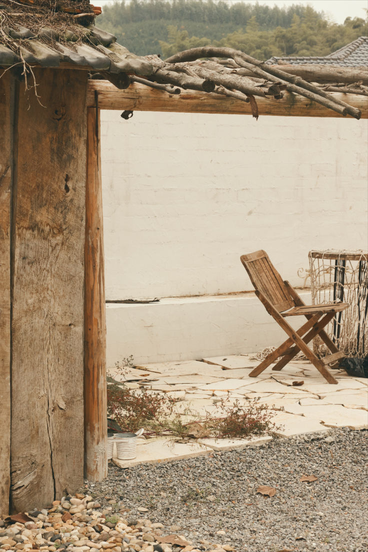 a wooden chair sitting in front of a white brick building with a wood frame and roof