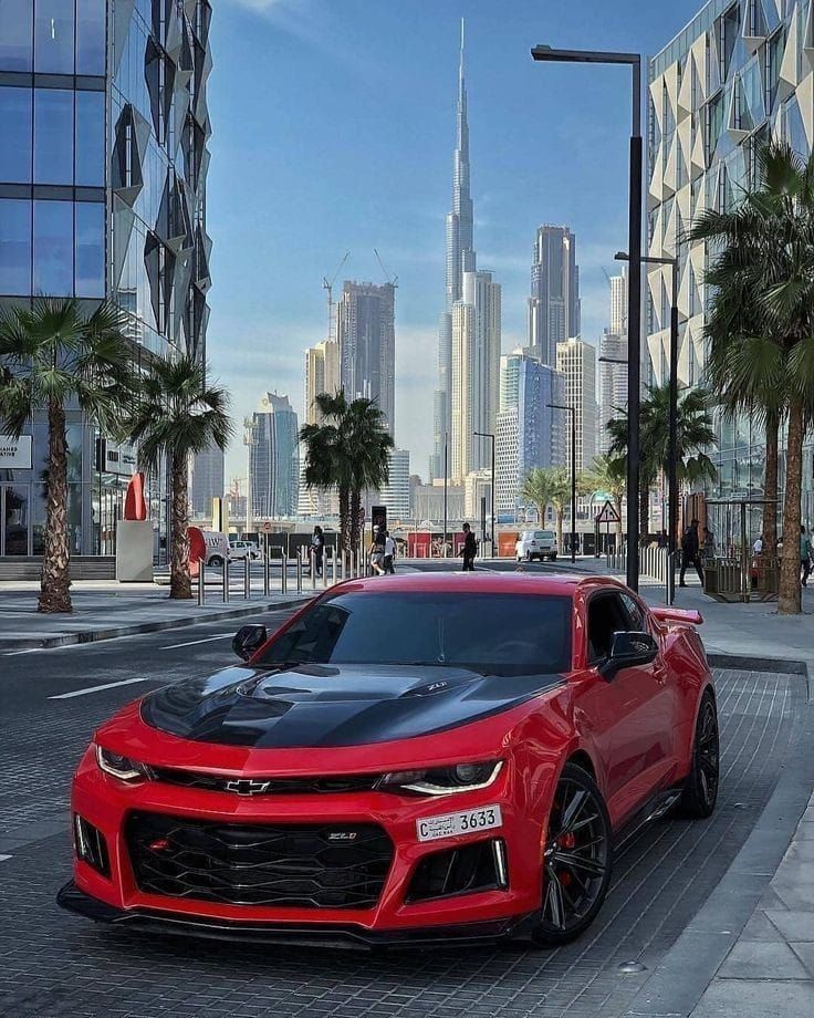 a red chevrolet camaro is parked on the side of the road in front of some tall buildings