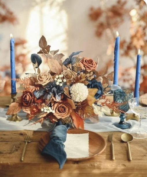 a bouquet of flowers sitting on top of a wooden table next to blue candles and napkins