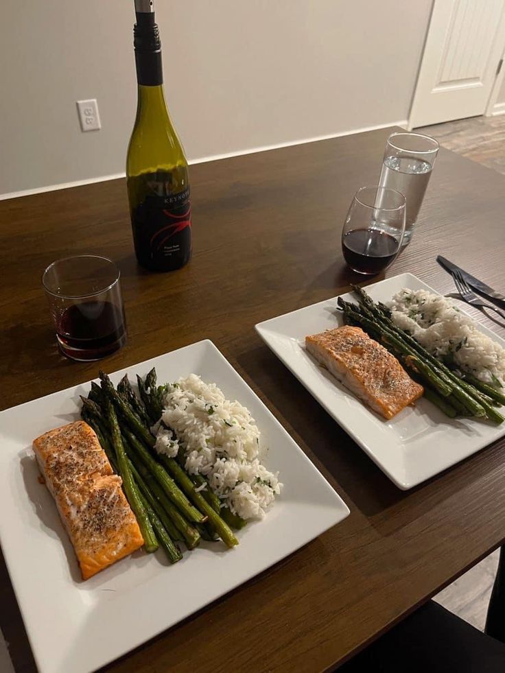 two white plates topped with salmon and asparagus next to a bottle of wine