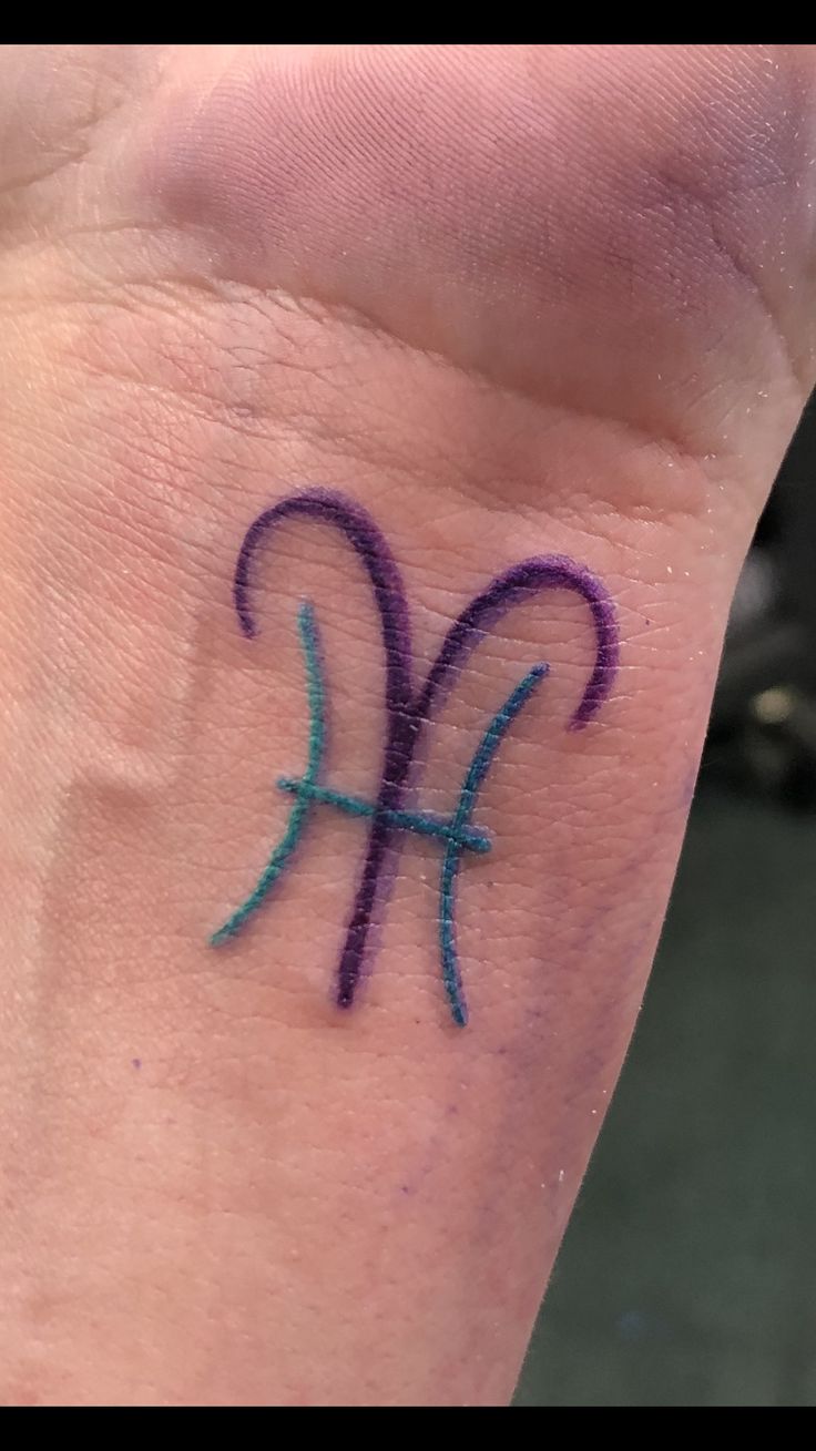 a small tattoo on the wrist of a person's left hand, with an aqua and purple symbol