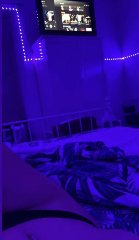 a bedroom with purple lighting and a flat screen tv mounted on the wall above the bed