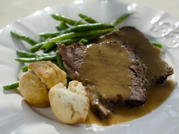 a white plate topped with meat and potatoes covered in gravy next to green beans