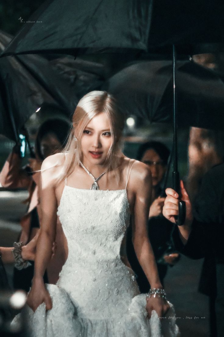 a woman in a white dress holding an umbrella and posing for the camera with other people behind her