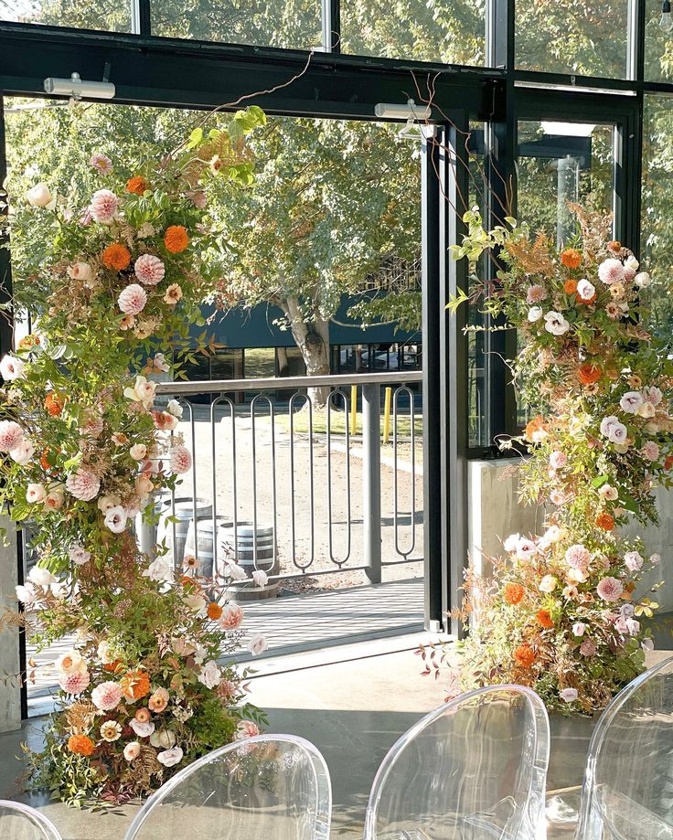 the chairs are covered with flowers and greenery in front of an open glass door