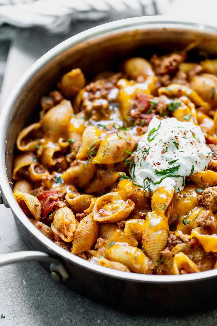 a skillet filled with pasta and meat covered in sour cream, parmesan